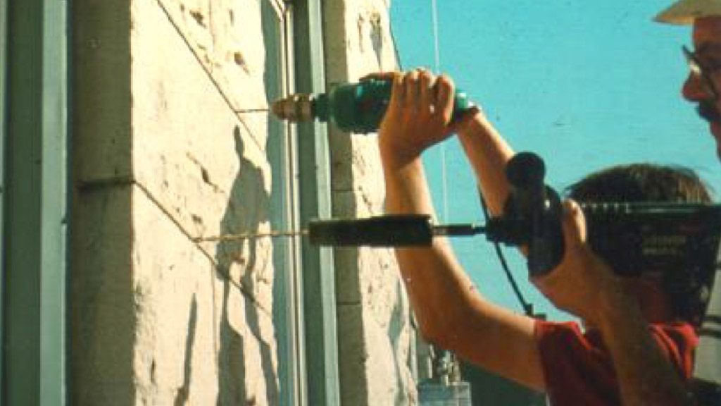Installation of helical ties in a stone veneer. The pilot hole is being drilled in the upper bed jointand a helical tie is being installed in the lower mortar joint. Installation of helical ties in a stone veneer. The pilot hole is being drilled in the upper bed jointand a helical tie is being installed in the lower mortar joint.