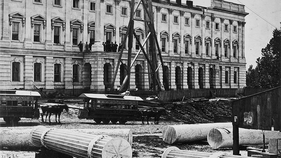 Shown is the north elevation of the Senate Extension with the balcony under construction. In the foreground are rough-turned column shafts and the finished fluted column shafts. The rough turning was done at the quarry, and all finished carving was done on site. c.1863.